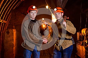 Two young guys in working uniform and protective helmets, shaking hands