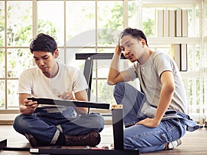 Dos joven a lindo asiático hombres intentar sobre el reunir muebles a conseguir confundido 