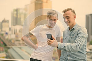 Two young handsome men with blond hair together against view of the city