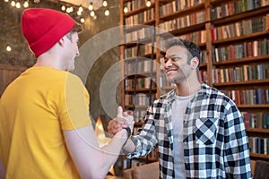 Two young handsome men looking glad shaking hands