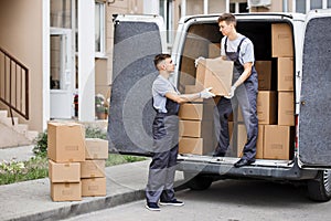 Two young handsome movers wearing uniforms are unloading the van full of boxes. House move, mover service