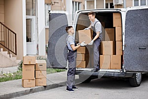 Two young handsome movers wearing uniforms are unloading the van full of boxes. House move, mover service