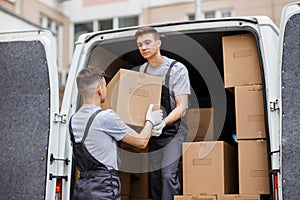 Two young handsome movers wearing uniforms are unloading the van full of boxes. House move, mover service