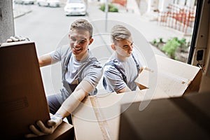 Two young handsome smiling movers wearing uniforms are unloading the van full of boxes. House move, mover service photo
