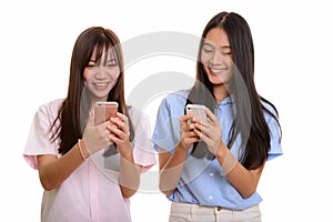 Two young happy Asian teenage girls smiling and using mobile pho