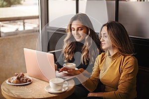 Two young happy attractive women business partners using at laptop at meeting in cafe