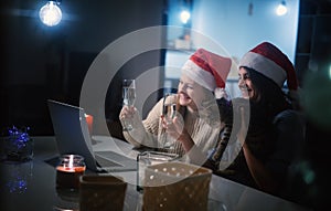 Two young happy beautiful women girlfriends lesbian couple with glasses of champagne in red santa hats celebrate new