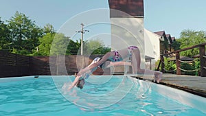 Two young happy blondes synchronously dive into outdoor pool. Slowmo