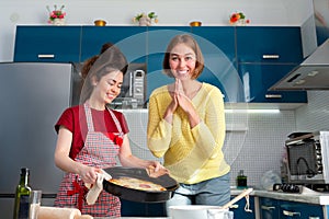 Two young happy caucasian women cooking in the kitchen. They made pizza together. Concept of family cooking and LGBT
