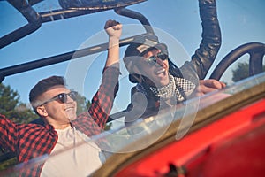 two young happy excited men enjoying beautiful sunny day while driving a off road buggy car