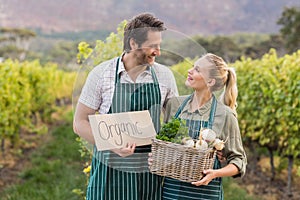 Two young happy farmers holding a sign and a basket of vegetables