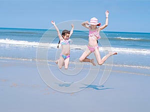 Two young happy girl having fun on tropical beach and jumping in swimsuit into the air on the sea coast at the day time