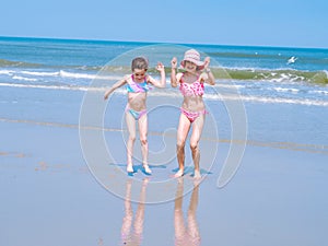 Two young happy girl having fun on tropical beach and jumping in swimsuit into the air on the sea coast at the day time