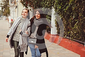 Two young happy girlfriends walking on city streets in casual fashion outfits