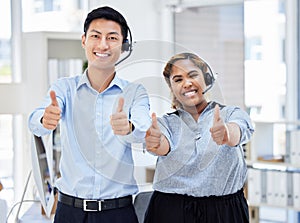 Two young happy male and female call center agents showing thumbs up while answering calls working in an office at work