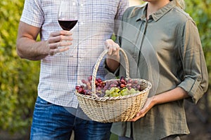 Two young happy vintners holding a basket of grapes and a glass of wine