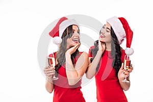Two young happy women celebrating in Christmas hat drink champange on white background.
