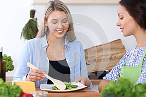 Two young happy women are cooking in the kitchen. Friends are having fun while preapering healthy and tasty meal