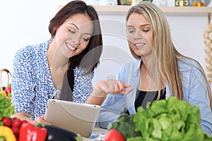 Two young happy women are making online shopping by tablet computer and credit card. Friends are going to cook in th