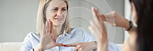 Two young happy women sitting on couch and making sign languages photo