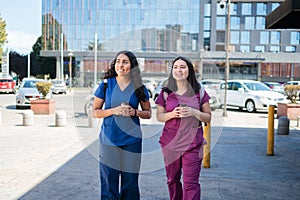 Two young hardworking latin nurses walking with cup of coffee after work. Female Healthcare workers leaving hospital