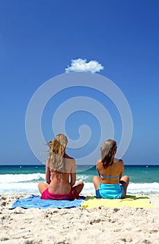 Two young, healthy women sitting on a sunny beach