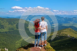 Two young hikers standing on top of a mountain and enjoying a beautiful valley view