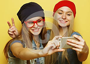 Two young hipster girls friends taking selfie over yellow background
