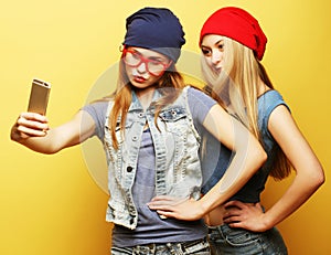 Two young hipster girls friends taking selfie over yellow background