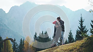 Two young hipsters traveling together in highlands. Happy person hugging and kissing while hiking on mountain or hill