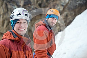 Two young ice climbers in sport helmets looking at us on ice background