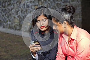 Two young Indian girls sitting and looking at their mobile, Pune