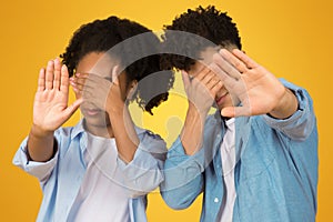 Two young individuals, a girl and a boy, playfully enact 'see no evil' with hands over eyes