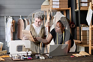 Two young intercultural seamstresses discussing new sketch of attire