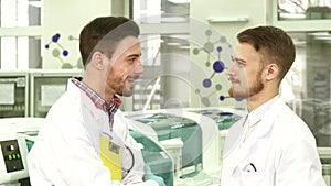 Two young lab technicians stand in the middle of the laboratory and talk
