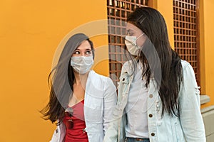 Two young Latinas wearing masks walking down the street