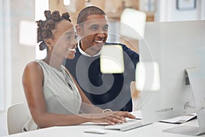 Two young male and female businesspeople using a desktop computer together in an office at work. African american