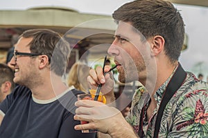 Two young male friends having fun, drinking cocktails and chatting with friends on terrace cafe in town