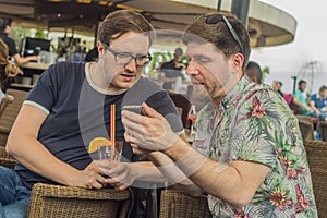 Two young male friends having fun, drinking cocktails and chatting with friends on terrace cafe in town