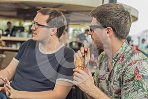 Two young male friends having fun, drinking cocktails and chatting with friends on terrace cafe in town