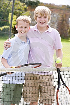 Two young male friends on tennis court smiling
