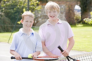 Two young male friends on tennis court smiling