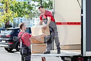 Two Young Male Movers Carrying Cardboard Boxes From Truck photo