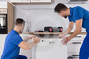 Two movers placing dishwasher in kitchen