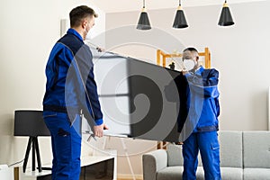 Two Young Male Movers In Uniform Placing Television