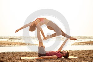 Two young man and beautiful woman on beach doing fitness yoga exercise together. Acroyoga element for strength and