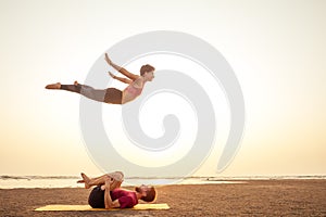 Two young man and beautiful woman on beach doing fitness yoga exercise together. Acroyoga element for strength and