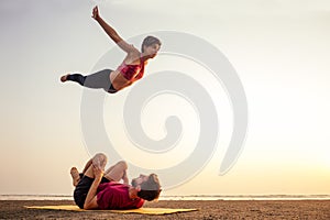 Two young man and beautiful woman on beach doing fitness yoga exercise together. Acroyoga element for strength and