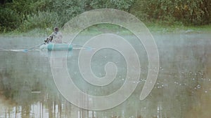 Two young man sitting in the rubber boat and rowing with paddles in the morning. Two male on the lake with fog on it.