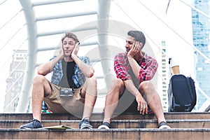 Two young man tired to find the place to go, throwing the map on the ground. Friends waiting for a tour guide